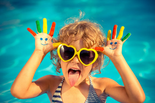 Cute kid in the pool doing faces with paint on her hands at summer party.