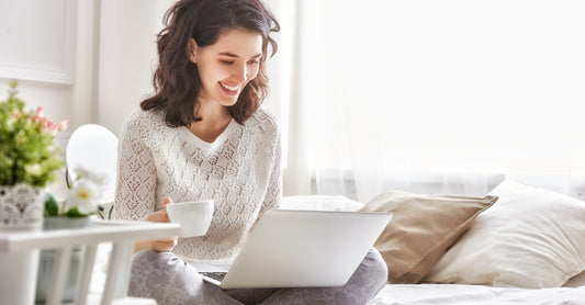 Woman working on a laptop sitting on her bed.